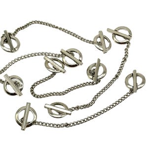 May include: A silver chain necklace with multiple circular pendant charms. Each charm has a horizontal bar across the center.