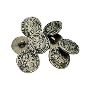 Może przedstawiać: Sześć srebrnych guzików z wypukłym wzorem profilu twarzy i tekstem wokół krawędzi. Guziki mają otwór w środku do szycia.