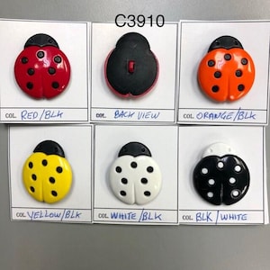 May include: Six ladybug buttons in different colours: red with black dots, orange with black dots, yellow with black dots, white with black dots, black with white dots, and a black back view. The buttons are labelled with the colour combinations: "RED/BLK", "ORANGE/BLK", "YELLOW/BLK", "WHITE/BLK", "BLK/WHITE", and "BACK VIEW". The buttons are labelled with the code "C3910".