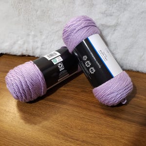 May include: Two skeins of lavender purple acrylic yarn. The yarn is labeled "Sport Yarn Acrylic Yarn 100% Acrylic Machine Washable."