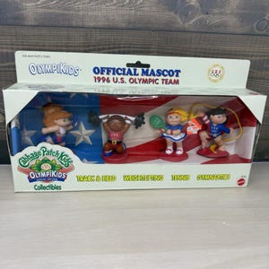 May include: A Cabbage Patch Kids Olympikids collectible set featuring four small figures in a box labeled Official Mascot 1996 U.S. Olympic Team. The figures represent track and field, weightlifting, tennis, and gymnastics with red, white, and blue accents.