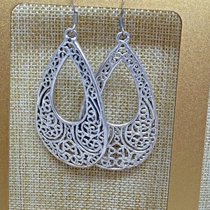 May include: A pair of silver-colored, openwork teardrop earrings. The earrings feature an intricate, swirling filigree design. The earrings hang from a simple hook.
