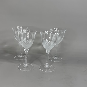 May include: Four clear glass wine glasses with a frosted leaf design on the bowl. The glasses have long stems and round bases. The background is a solid gray.
