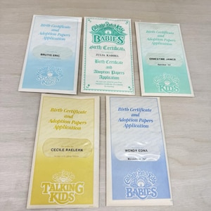 May include: Five rectangular Cabbage Patch Kids birth certificate and adoption papers application documents. The papers feature various pastel colors including blue, green, and yellow, with printed text and logos for Splashin Kids, Babies, and Talking Kids.