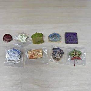 May include: A collection of nine Cabbage Patch Kids metal pins in various shapes and colors, including gold, silver, and purple tones. Several pins feature the Cabbage Patch Kids logo, character illustrations, and text such as 2002 Reflections of the Past.