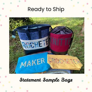 Puede incluir: Una colección de cuatro bolsas de tela que incluye un bolso grande azul estampado con el texto CROCHETER, una bolsa de cubo con cordón rojo oscuro con el texto KNITTER, una bolsa azul brillante con el texto MAKER y una bolsa amarilla con el texto CROCHETER.