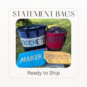 May include: A collection of four fabric bags including a blue patterned tote with the text CROCHETER, a maroon drawstring bag labeled KNITTER, a bright blue pouch labeled MAKER, and a yellow pouch with the text CROCHETER in floral letters.