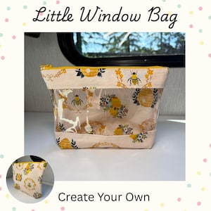May include: A Little Window Bag with a yellow zipper, featuring a cream-colored fabric with a bee and beehive pattern and a clear vinyl center panel. The bag is displayed with a smaller matching pouch in the corner, labeled Create Your Own.