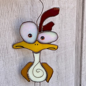 May include: A stained glass bird with a yellow body, white eyes, and a red crest. The bird has a long neck and a long, thin leg.
