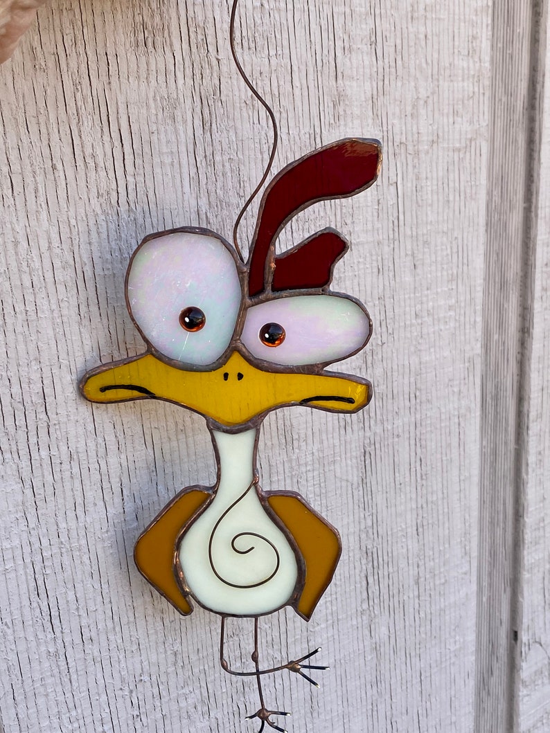 May include: A stained glass bird with a yellow body, white eyes, and a red crest. The bird has a long neck and a long, thin leg.