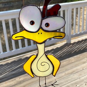 May include: A stained glass bird with large, white eyes, a yellow body, and a red crest. The bird has a long, thin neck and legs.