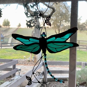 May include: A teal blue stained glass dragonfly with black wire wings and a beaded tail hanging from a black wire vine with leaves.