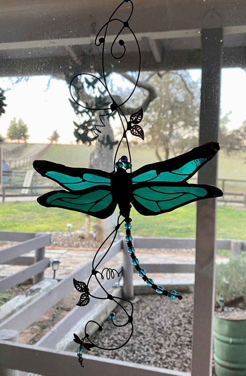 May include: A teal blue stained glass dragonfly with black wire wings and a beaded tail hanging from a black wire vine with leaves.