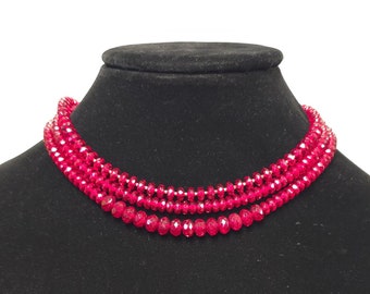 May include: A three-strand necklace made of bright red faceted beads. The necklace is displayed on a black velvet mannequin bust.