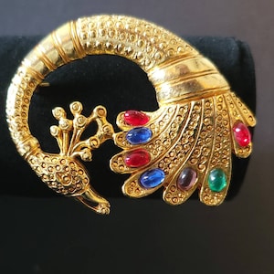 May include: A gold-tone peacock brooch with colorful rhinestones. The peacock's tail feathers are spread out and adorned with red, blue, and green stones.