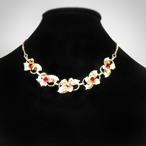 Könnte beinhalten: Eine goldene Halskette mit roten Blumenakzenten. Die Halskette ist aus Metall und hat ein Gliederketten-Design. Die Blumen sind aus Metall und haben rote Steine in der Mitte.