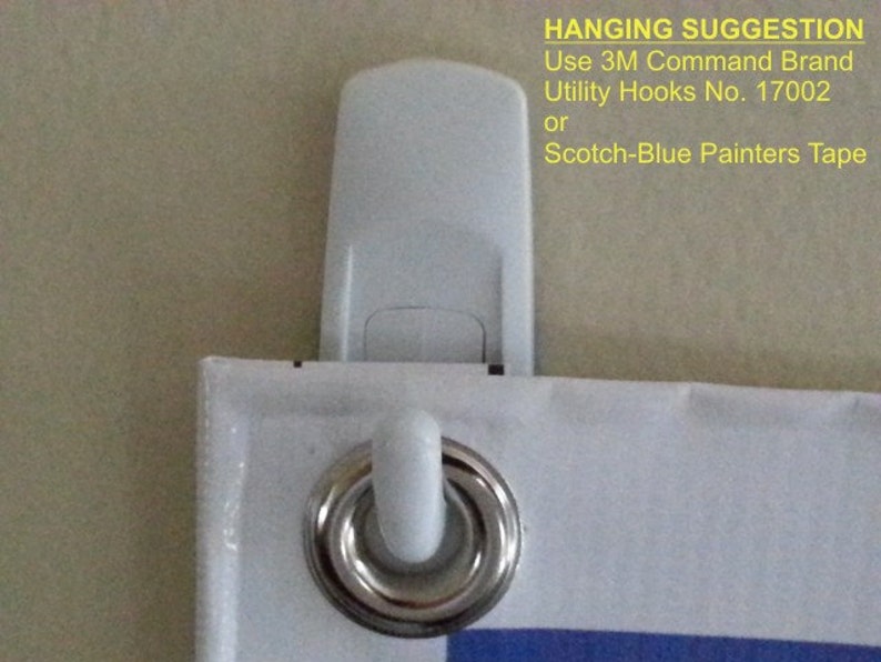 May include: Close-up of a white 3M Command Brand Utility Hook attached to a banner with a metal grommet. The banner has a white border and blue accents. Text on the image suggests hanging options.
