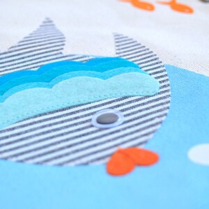 May include: A blue and white striped fish with a blue, turquoise, and light blue felt wave design. The fish has a white button eye and a red felt mouth.