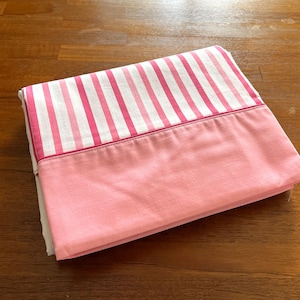 May include: Pink and white striped bed sheet with a solid pink hem.