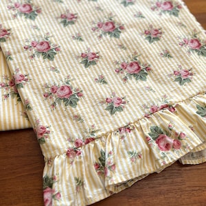 May include: A yellow and white striped tablecloth with a ruffled edge and a floral pattern of pink roses.