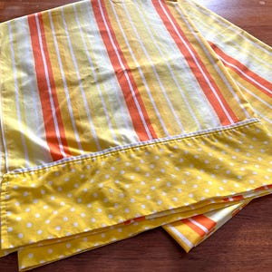 May include: A yellow and orange striped fitted sheet with a white polka dot border. The sheet is made of cotton and is soft and comfortable.