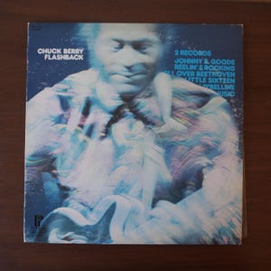 以下が含まれることがあります： チャック・ベリーの「フラッシュバック」のアルバムカバー。青と白を基調とした、ぼやけた芸術的な男性のイメージが特徴です。「Chuck Berry Flashback」や「Johnny B. Goode」などの曲名がテキストに含まれています。
