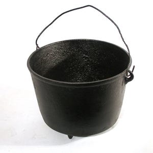 May include: A black cast iron pot with a wire handle and three legs. The pot is empty and has a rough, textured surface.