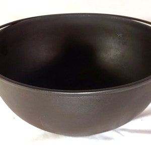 May include: A black cast iron cauldron with two handles. The cauldron is round and has a smooth surface.