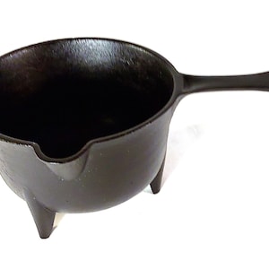 May include: A black cast iron pot with a handle and three legs. The pot is designed for melting wax or chocolate.