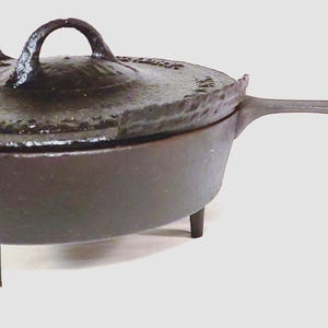 May include: A cast iron Dutch oven with a lid and handle. The pot has three short legs and a long handle. The lid has a loop handle and a textured surface. The pot is dark brown.