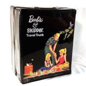 May include: A black Barbie & Skipper Travel Trunk with a glossy finish. The trunk features a vintage illustration of Barbie, Skipper, and a man having a picnic. The text "Barbie & Skipper. Travel Trunk" is printed on the front.