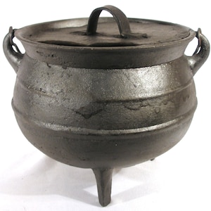 May include: A black cast iron pot with a lid and three legs. The pot has two handles on the sides and a single handle on the lid.