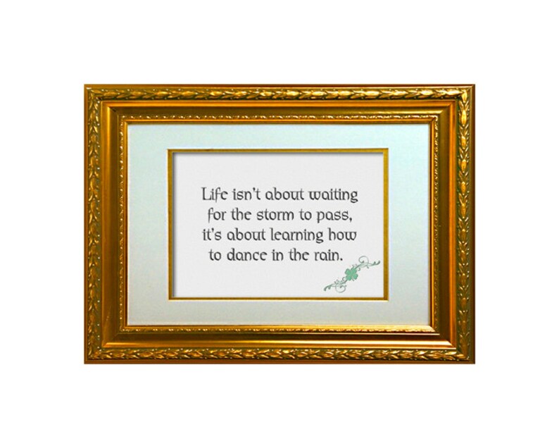 May include: A framed inspirational quote in a gold frame. The quote reads: "Life isn't about waiting for the storm to pass, it's about learning how to dance in the rain."