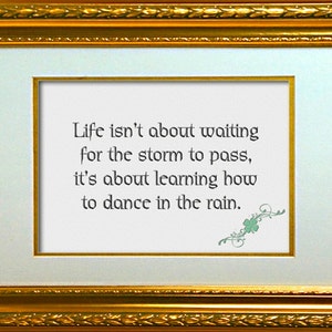 May include: A framed print with a gold frame and a white mount. The print features a quote about life and dancing in the rain. The quote reads: "Life isn't about waiting for the storm to pass, it's about learning how to dance in the rain."