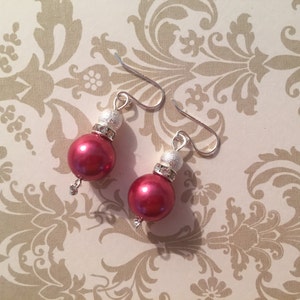 May include: A pair of earrings with silver hooks and red pearl-like beads. Each bead has a silver accent with a clear rhinestone.