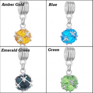 May include: Four silver charm beads with different coloured crystal balls. The beads are labelled "Amber Gold", "Blue", "Emerald Green", and "Green".