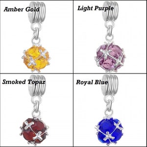 May include: Four silver charm beads with different coloured crystal balls. The beads are labelled "Amber Gold", "Light Purple", "Smoked Topaz", and "Royal Blue".