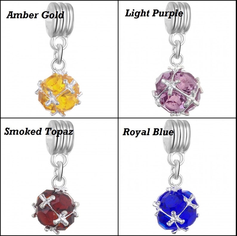 May include: Four silver charm beads with different coloured crystal balls. The beads are labelled "Amber Gold", "Light Purple", "Smoked Topaz", and "Royal Blue".