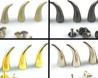 May include: Four sets of three metal horn-shaped studs with screws. The horns are in gold, silver, antique gold, and black.