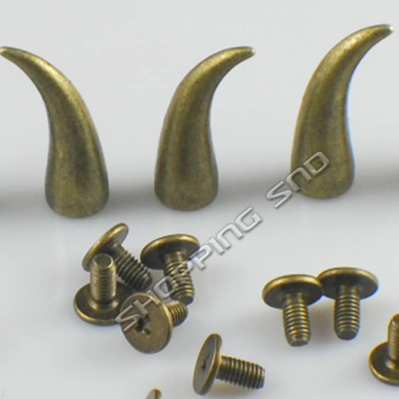 K&ouml;nnte beinhalten: Drei antike, goldfarbene, metallene Hornverzierungen mit Schraubr&uuml;cken. Die Verzierungen sind etwa 5 cm lang. Es sind auch mehrere Schrauben enthalten.