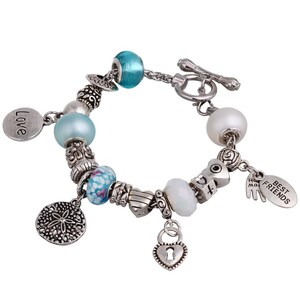 Puede incluir: Un brazalete de plata con abalorios azules y blancos, encantos y un cierre de plata. Los encantos incluyen un corazón con un ojo de cerradura, una concha, un búho pequeño y un encanto que dice "Mejores Amigos".
