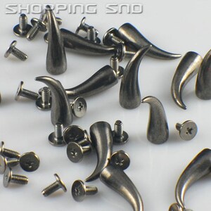 K&ouml;nnte beinhalten: Eine Sammlung silberfarbener Metall-Horn-Nieten mit Schrauben. Die Nieten sind etwa 2,5 cm lang und haben eine spitze Spitze. Sie sind ideal, um Kleidung, Taschen oder anderen Accessoires einen Punk-Rock- oder Gothic-Stil zu verleihen.