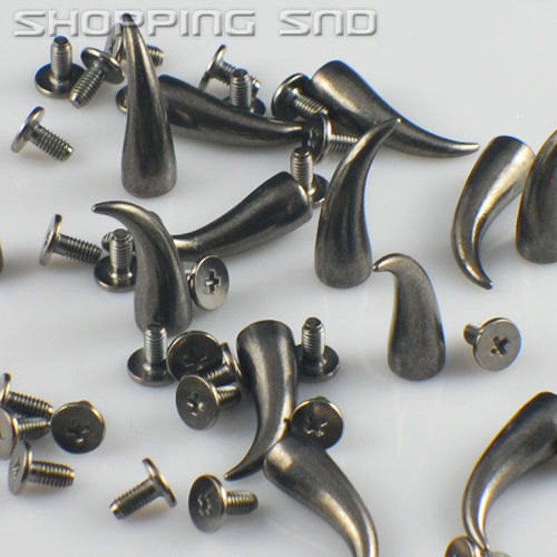 K&ouml;nnte beinhalten: Eine Sammlung silberfarbener Metall-Horn-Nieten mit Schrauben. Die Nieten sind etwa 2,5 cm lang und haben eine spitze Spitze. Sie sind ideal, um Kleidung, Taschen oder anderen Accessoires einen Punk-Rock- oder Gothic-Stil zu verleihen.