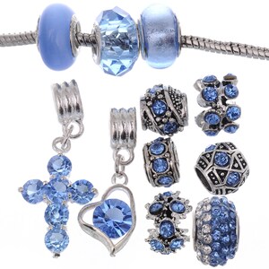 May include: A set of blue and silver charm beads for a bracelet or necklace. The beads feature various designs, including a cross, a heart, and a star. The beads are made of metal and have blue crystals.