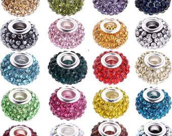 May include: Assortment of 18 round, silver-toned, rhinestone-encrusted beads. The beads are in various colours, including red, green, blue, purple, gold, and clear.