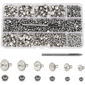 May include: A clear plastic organizer filled with various sizes of silver-toned metal rivets and rhinestone embellishments. Several individual rivets and eyelets are displayed below. A metal setting tool is also included.