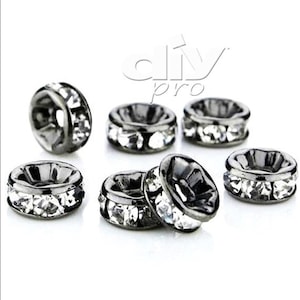 Puede incluir: Siete anillos de metal negro con detalles de diamantes de imitación transparentes. Los anillos tienen un diámetro de aproximadamente 1,25 cm.