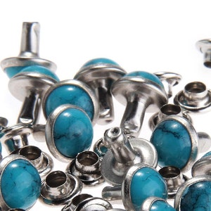 May include: A close-up of turquoise and silver metal studs. The studs have a round turquoise stone in the centre and a silver metal rim. The studs are used for crafting and decorating.