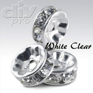 Puede incluir: Tres tapas de cuentas plateadas con cristales de cristal transparentes alrededor del borde. Blanco Claro.
