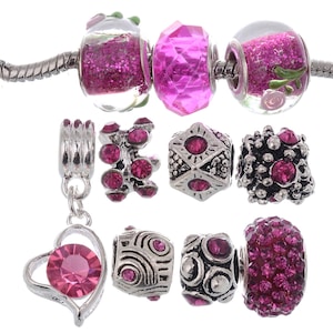 May include: A set of pink and silver charm beads for a bracelet. The beads are made of glass, metal, and crystals. Some beads have a sparkly finish.